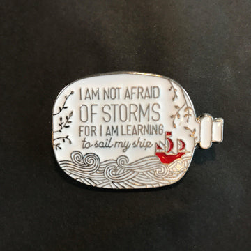 Das Produktbild zeigt einen weißen Pin in Form einer bauchigen Flaschenpost, in dessen Innerem mit silbernen Buchstaben der Spruch "I am not afraid of storms for I am learning to sail my ship" steht. Darunter sind silberne Wellen und rechts ein rotes Schiff, daneben ein paar silberne Zweige mit silbernen Blättern angedeutet.